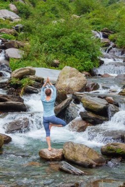 Yogadaki kadın, Vrikshasana ağacı, şelalede poz veriyor.