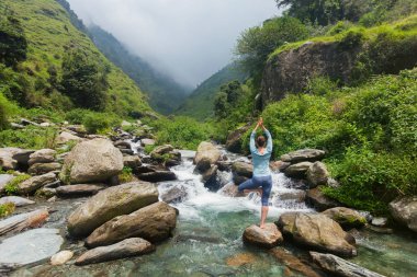 Yogadaki kadın, Vrikshasana ağacı, şelalede poz veriyor.