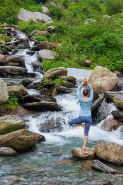 Yogadaki kadın, Vrikshasana ağacı, şelalede poz veriyor.