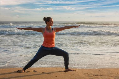 Kadının üzerinde yoga asana Virabhadrasana 1 savaşçı poz plajda yapması