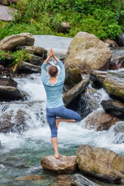 Yogadaki kadın, Vrikshasana ağacı, şelalede poz veriyor.