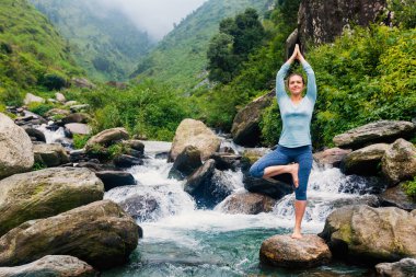 Yogadaki kadın, Vrikshasana ağacı, şelalede poz veriyor.