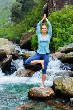 Yogadaki kadın, Vrikshasana ağacı, şelalede poz veriyor.