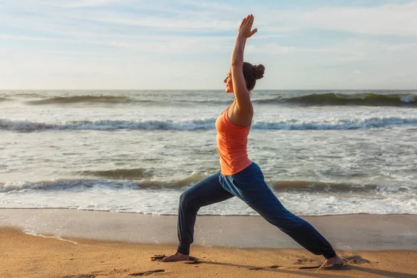 Mulher fazendo ioga asana Virabhadrasana 1 guerreiro dose na praia em — Fotografia de Stock