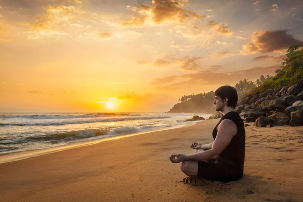 Young sporty fit man doing yoga meditating on tropical beach — Stock Photo, Image