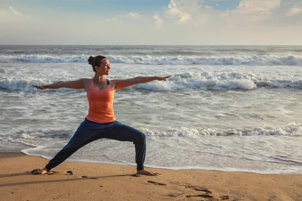 Vrouw doet yoga asana Virabhadrasana 1 Warrior vormen op strand op — Stockfoto
