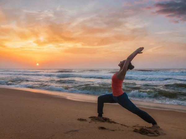 Vrouw doet yoga asana Virabhadrasana 1 Warrior vormen op strand op — Stockfoto