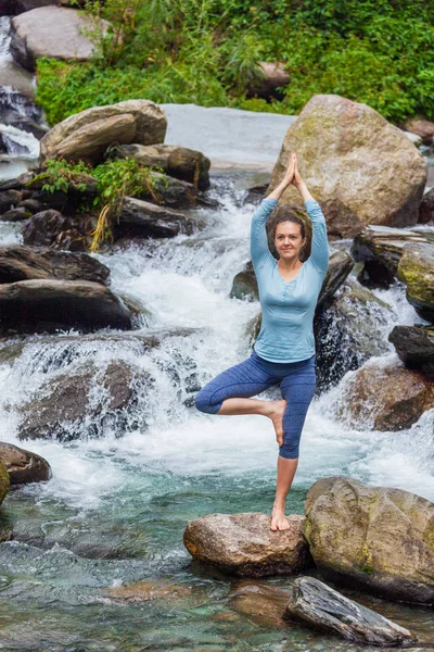 Yogadaki kadın, Vrikshasana ağacı, şelalede poz veriyor.