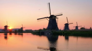 Hollanda 'nın ünlü turizm sahası Kinderdijk' te kırsal alandaki yel değirmenleri dramatik gökyüzü ve su yansıması ile gün batımında