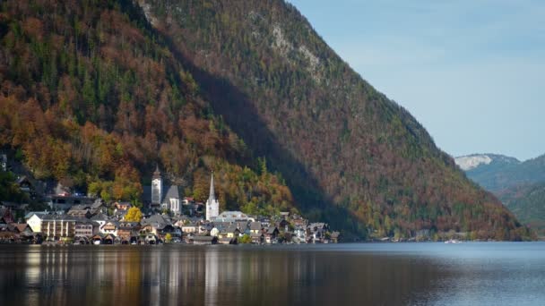 秋天落在奥地利高山阿尔卑斯山中著名的旅游胜地 宁静的哈尔斯塔特镇 大教堂 当地的房屋 高山上树上的金黄的叶子 映衬在平静的湖水里 — 图库视频影像