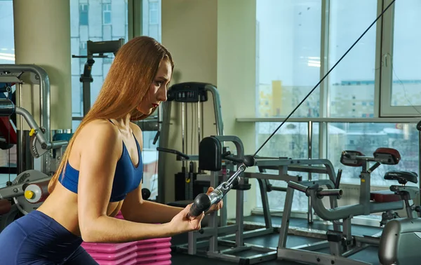 sporty woman builds muscle arms and chest on the simulator