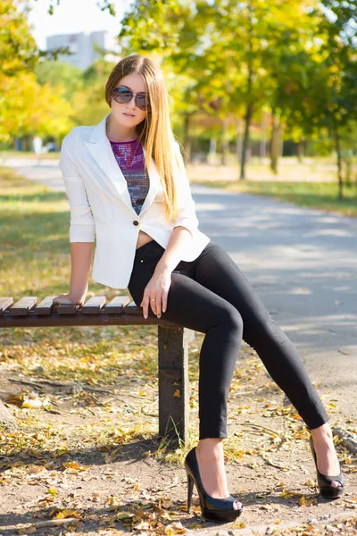 Beautiful young woman in black pants and white jacket looking at camera in park