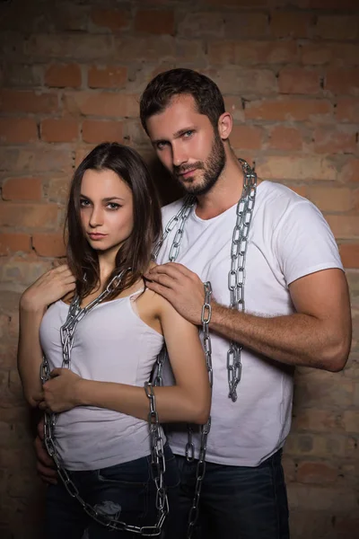 热情的年轻夫妇在白色的 T恤摆在砖墙前的铁链 看着相机 — 图库照片