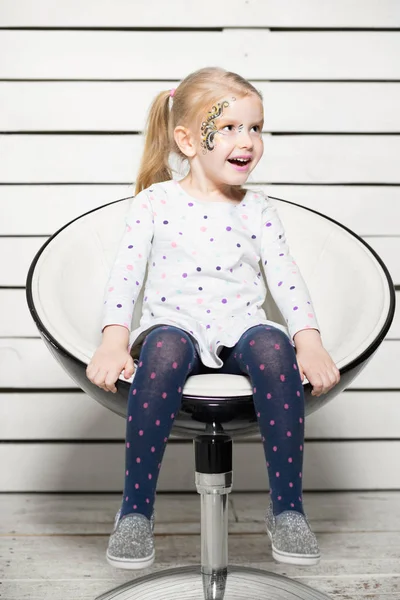 little girl with colorful face sitting on chair