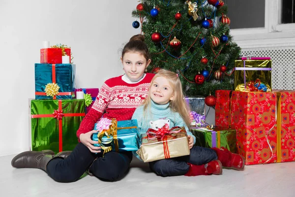 スタジオで祝いクリスマス ツリーのそばに座ってプレゼントを持つ女の子 — ストック写真