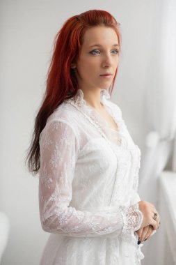 Kırmızı saçlı, zarif beyaz elbiseli genç bayan.