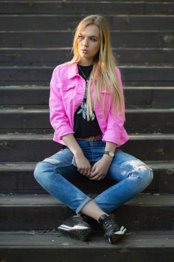 Genç, güzel sarışın kadın merdivenlerde oturuyor.