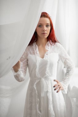Kırmızı saçlı, zarif beyaz elbiseli genç bayan.