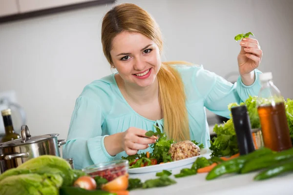 Young woman decorating salad with herbs in kitchen — Stock Photo, Image