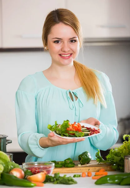 Ευτυχισμένο κορίτσι κρατώντας πιάτο με σαλάτα στην κουζίνα του σπιτιού — Φωτογραφία Αρχείου