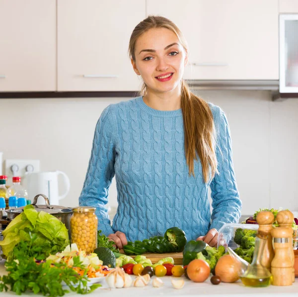 若いです女性で青プルオーバー調理野菜室内 — ストック写真