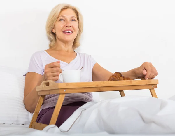 Mujer madura disfrutando del desayuno en la cama —  Fotos de Stock