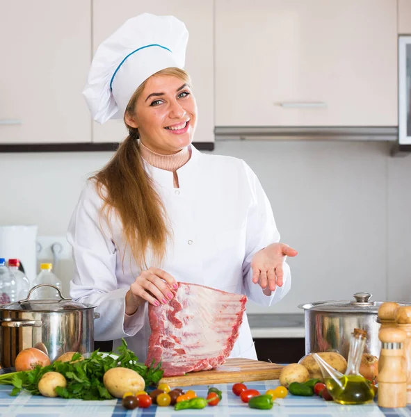 Professional female cook with ribcage in kitchen — Stock Photo, Image