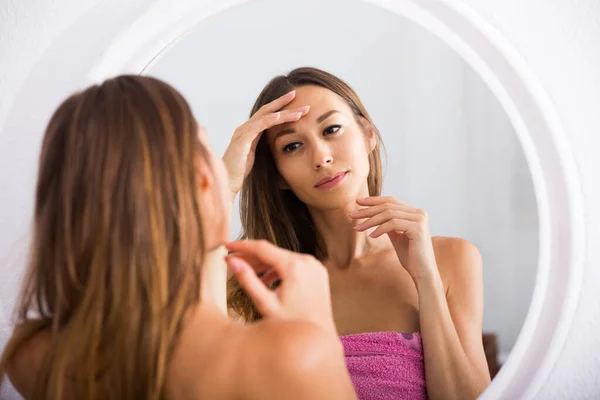 Жінка досліджує своє обличчя, дивлячись на нього у дзеркало — стокове фото
