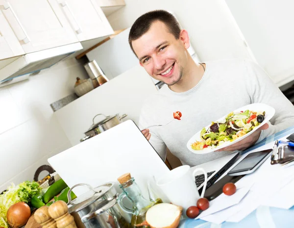 Επιτυχημένος άνθρωπος δοκιμάζοντας λαχανικά πιάτο κοντά στο laptop — Φωτογραφία Αρχείου