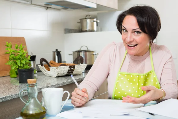 Šťastná hospodyňka s bankovními papíry v kuchyni — Stock fotografie