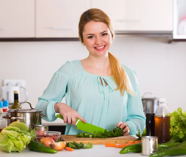 Jovem mulher cortando alface e ervas na cozinha — Fotografia de Stock