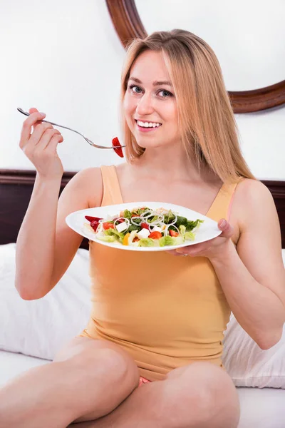 Blond woman in underwear sitting in the bed and enjoying a salad — Stock Photo, Image