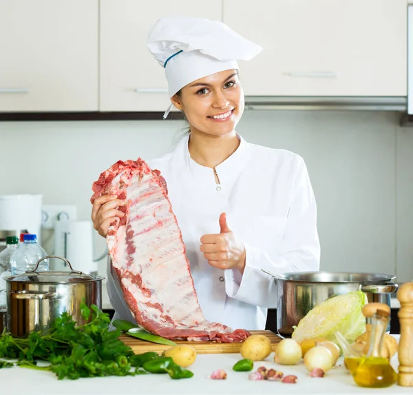 Chef féminin positif travaillant avec des côtes de porc — Photo