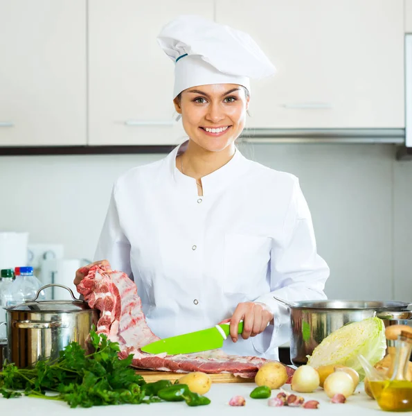 Chef féminin positif travaillant avec des côtes de porc — Photo