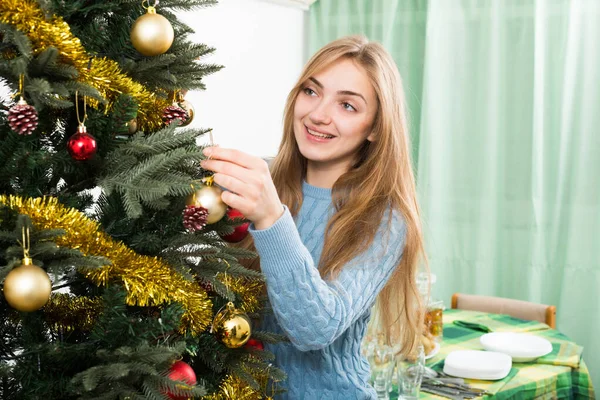 Молода жінка прикрашає ялинку і посміхається вдома — стокове фото