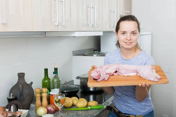 キッチンでの調理のウサギの肉と若い女性持株木材を笑顔の肖像画 — ストック写真