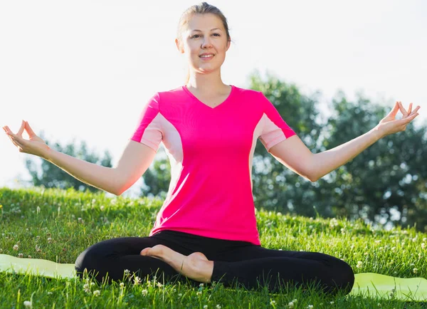 ピンクのTシャツの女性が座って公園で瞑想をしています — ストック写真
