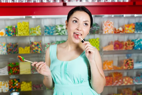 在糖果店吸棒棒糖的年轻女人 — 图库照片