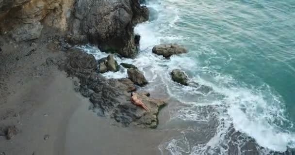 Оголена струнка дівчина позує витончено на скелі біля блакитного моря — стокове відео