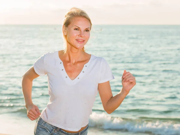 Mulher Adulta Sorridente Camiseta Branca Está Correndo Praia Perto Oceano — Fotografia de Stock