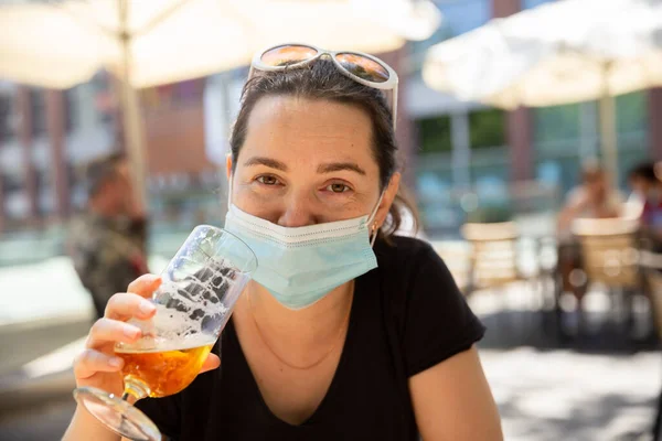 Kvinna i skyddande mask njuter av öl på utomhus bar terrass — Stockfoto
