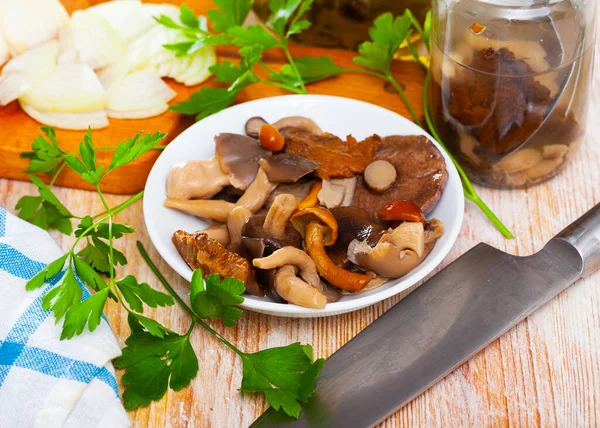 Различные консервированные грибы, лук и зелень на деревянном столе — стоковое фото
