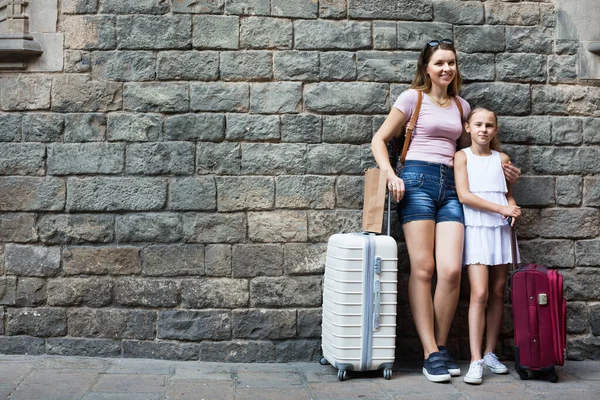 Mujer y niña viajera con la maleta apoyada contra la pared de piedra —  Fotos de Stock