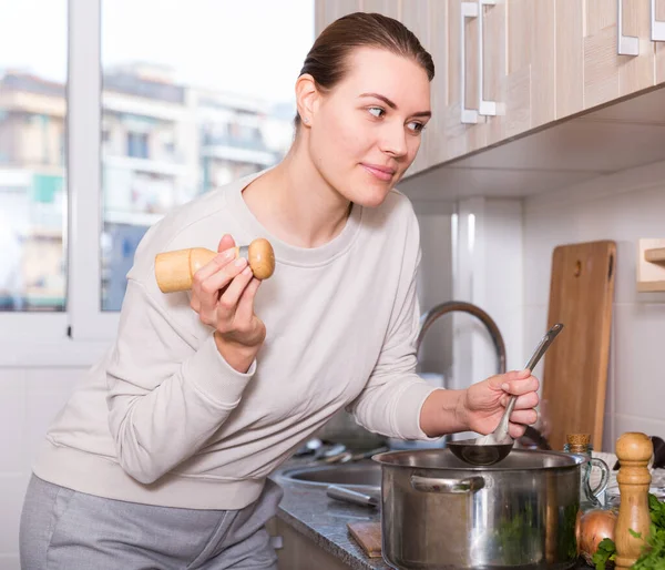 Femme au foyer cuisine la soupe dans la casserole et le sel dans la cuisine — Photo