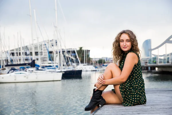 Joven mujer atractiva turista sentado en el muelle con veleros en el fondo —  Fotos de Stock