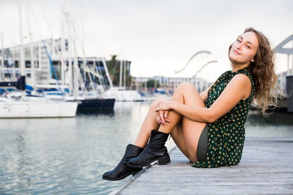 Joven mujer atractiva turista sentado en el muelle con veleros en el fondo —  Fotos de Stock