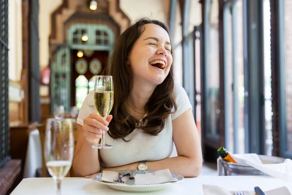 Smějící se žena se sklenkou vína u stolu v restauraci — Stock fotografie