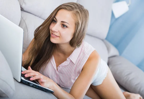 Chica acostada en el sofá con el ordenador portátil —  Fotos de Stock