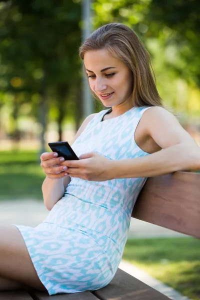 Meisje zitten op een bank en met behulp van telefoon in park — Stockfoto