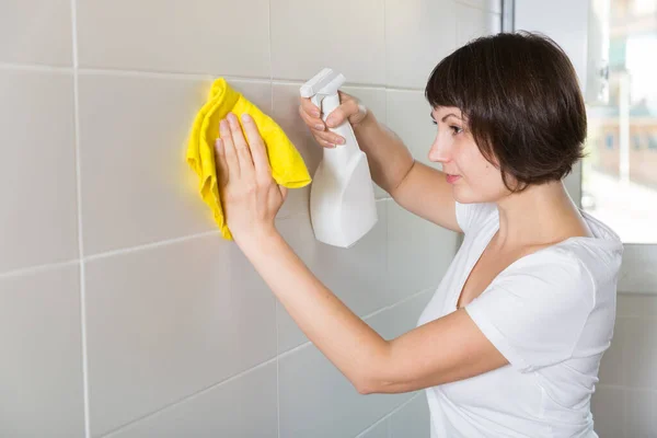 Vrouw met schoonmaakmiddel tegelwand — Stockfoto